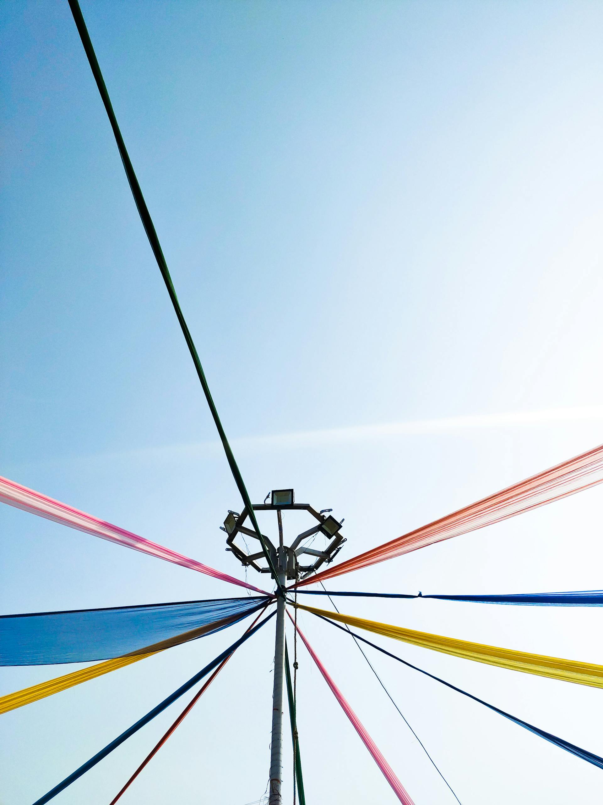 Vibrant multicolored ribbons on a maypole set against a clear blue sky during a spring festival.